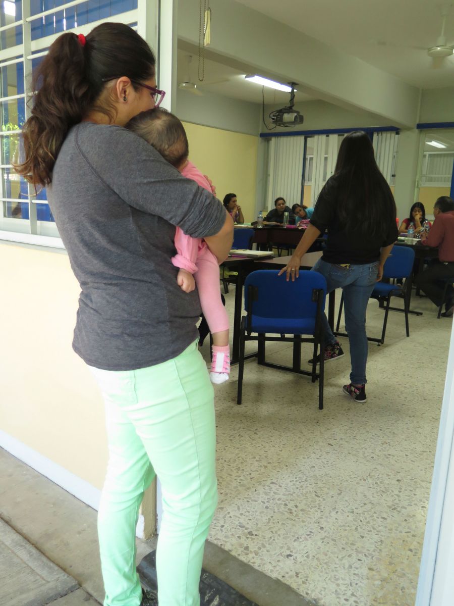 Nuestra cultura ensalza mucho la maternidad pero no brinda los medios necesarios para que ésta se realice en las mejores condiciones. En este sentido, hay muchas estudiantes mamás que tienen que ir a la escuela con sus bebés. En el caso de esta foto, la joven madre tiene que salirse del salón cuando la bebé se pone inquieta. Esta situación representa una desventaja frente a sus demás compañeros y compañeras.